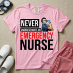 A retro ER nursing t-shirt featuring the bold text "NEVER UNDERESTIMATE AN EMERGENCY NURSE" alongside a vintage graphic of a masked nurse flexing her arm in a classic Rosie the Riveter pose