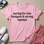 A minimalist nursing t-shirt featuring the text "caring for tiny humans & strong mamas" written in a retro white serif font.