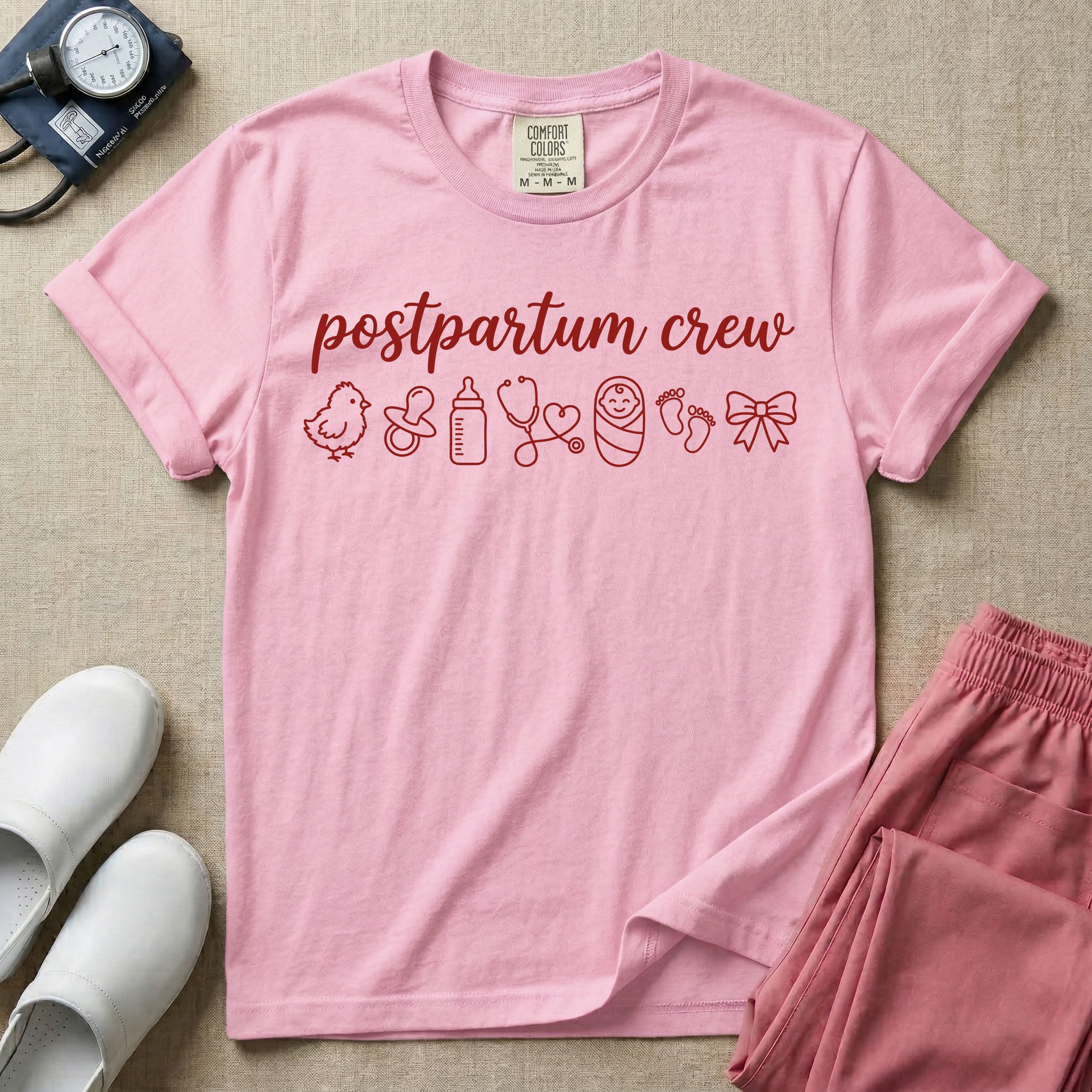 A t-shirt featuring the lowercase text postpartum crew in a cursive script font above a horizontal row of minimalist line-art icons including a baby chick, a pacifier, a baby bottle, a heart-shaped stethoscope, a swaddled baby, baby footprints, and a ribbon bow.