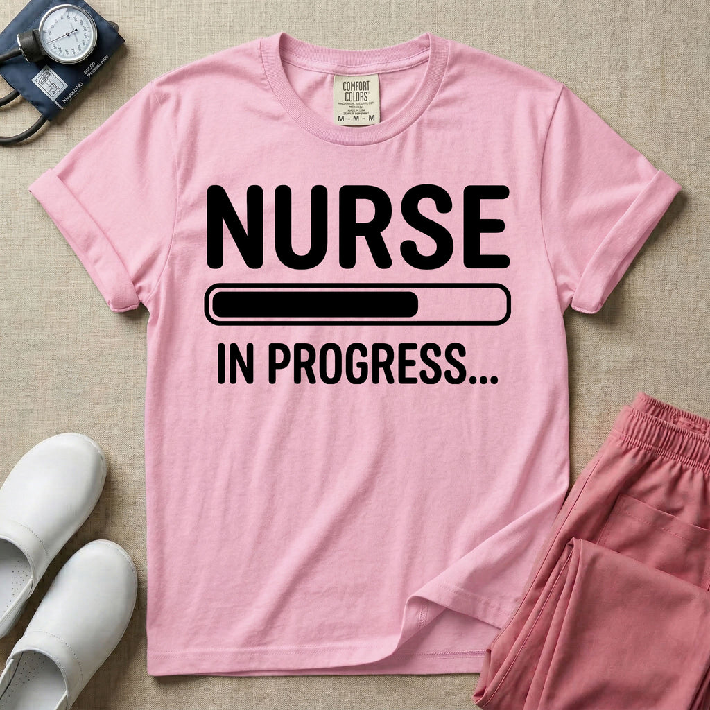General nursing student t-shirt featuring a white loading bar graphic and the text "NURSE IN PROGRESS..." on a dark gray garment, in blossom color.