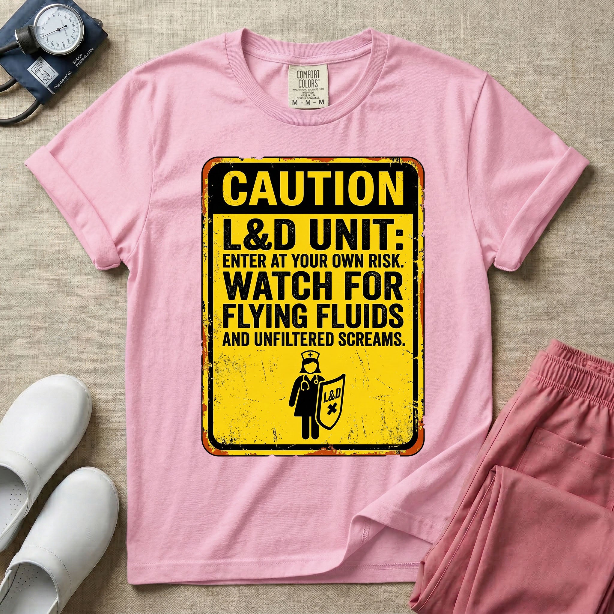 A humorous graphic tee for labor and delivery nurses featuring a distressed caution sign design with the text "CAUTION L&D UNIT: ENTER AT YOUR OWN RISK. WATCH FOR FLYING FLUIDS AND UNFILTERED SCREAMS." above a stick figure nurse holding a shield.