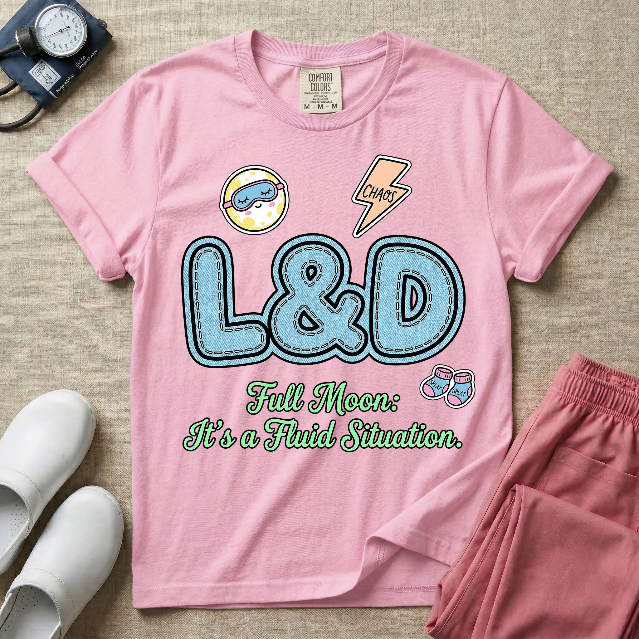A humorous Labor and Delivery nurse graphic featuring large, light blue varsity-style letters spelling L&D with a pink dashed outline, surrounded by small patch-like icons of a baby and a lightning bolt, sitting above cursive text that reads Full Moon: It's a Fluid Situation.
