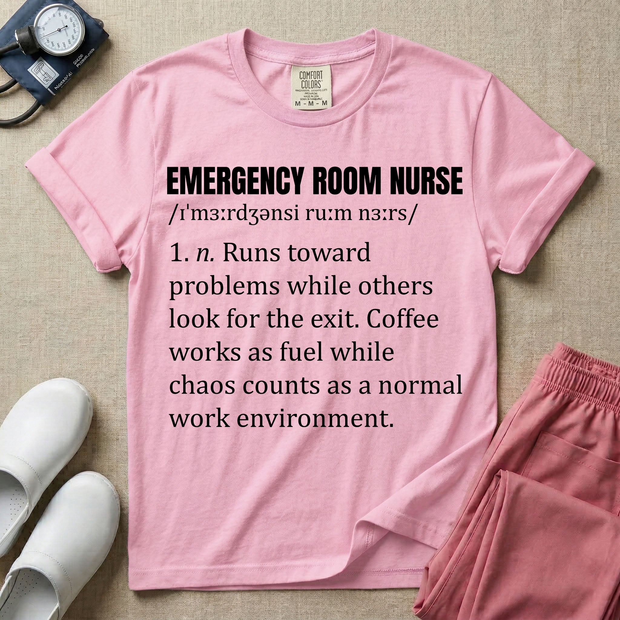 A minimalist t-shirt for emergency room nurses featuring a dictionary definition graphic for the term "EMERGENCY ROOM NURSE" with a phonetic pronunciation and a humorous description about running toward problems, using coffee as fuel, and thriving in chaos.