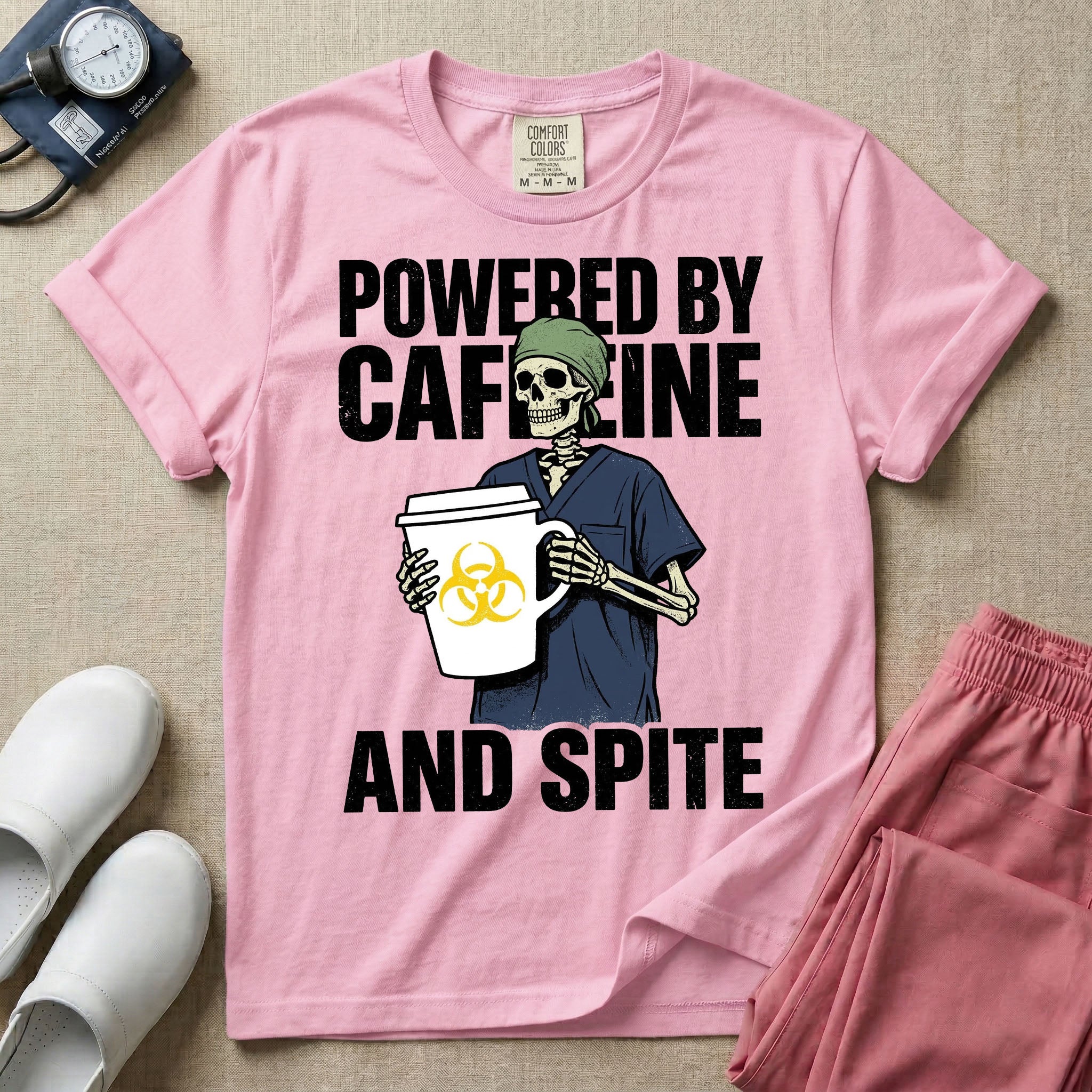 A humorous graphic for general nursing featuring an illustration of a skeleton wearing a green scrub cap and dark blue scrubs, holding a large white coffee cup with a yellow biohazard symbol, with the stacked text 'POWERED BY CAFFEINE' above it and 'AND SPITE' below it.