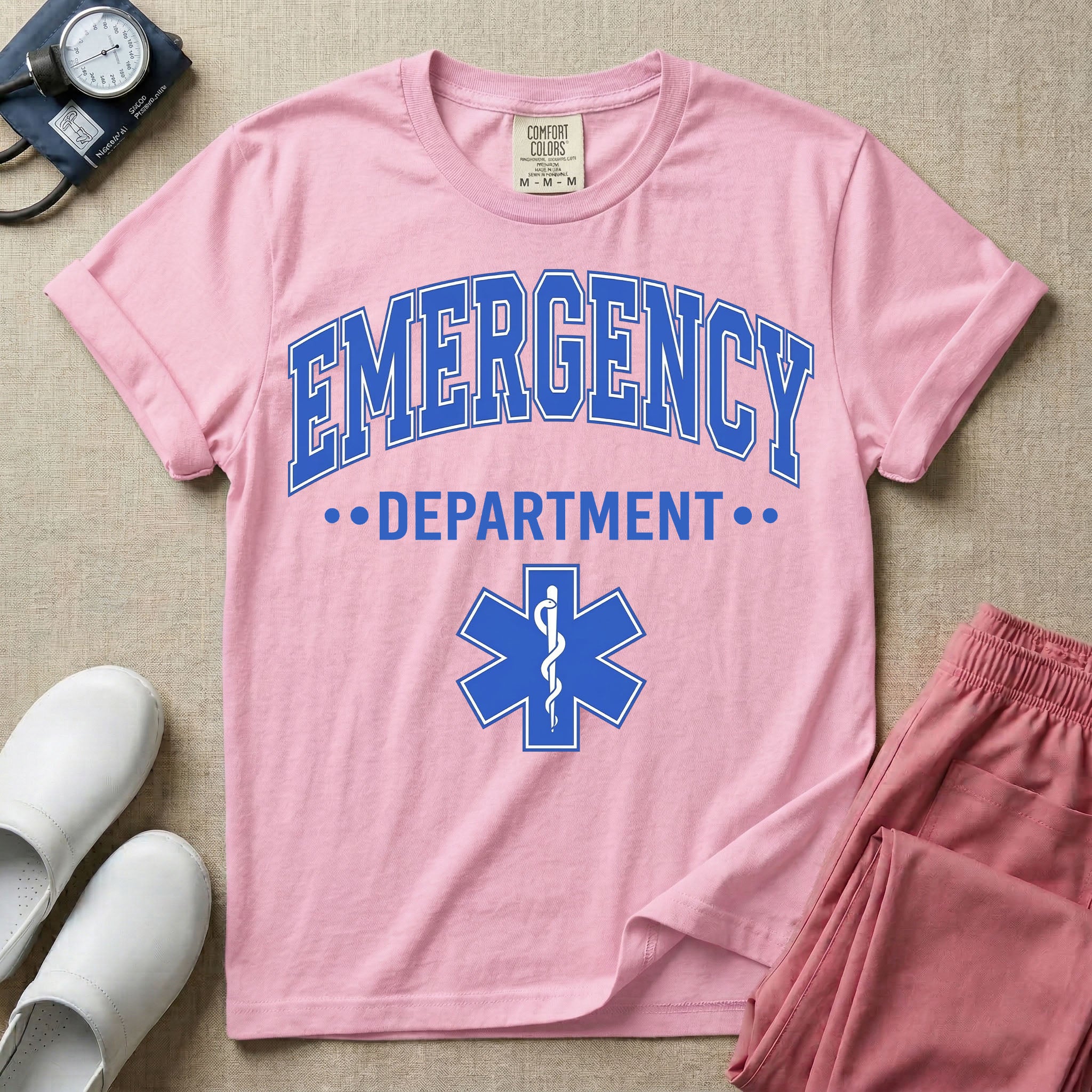 A classic varsity-style t-shirt for emergency room nurses featuring the word "EMERGENCY" in a large, arched blue collegiate font above the word "DEPARTMENT", centered over a blue Star of Life medical symbol.