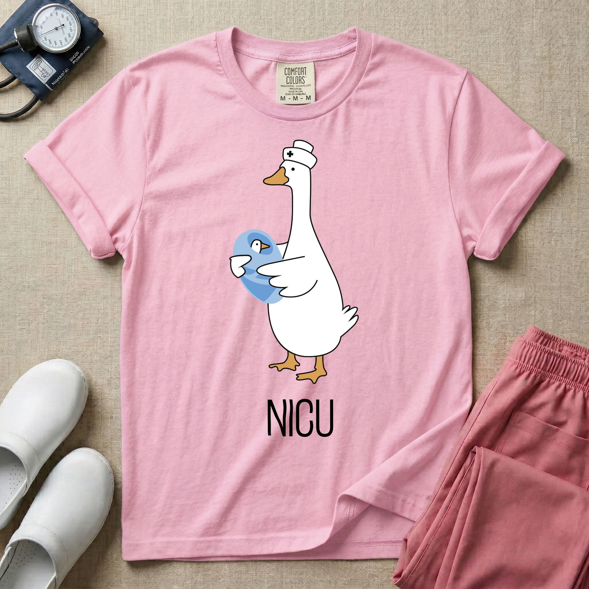 A t-shirt featuring an illustration of a white silly goose wearing a nurse's cap and holding a baby goose swaddled in a blue blanket, with the text NICU printed below.