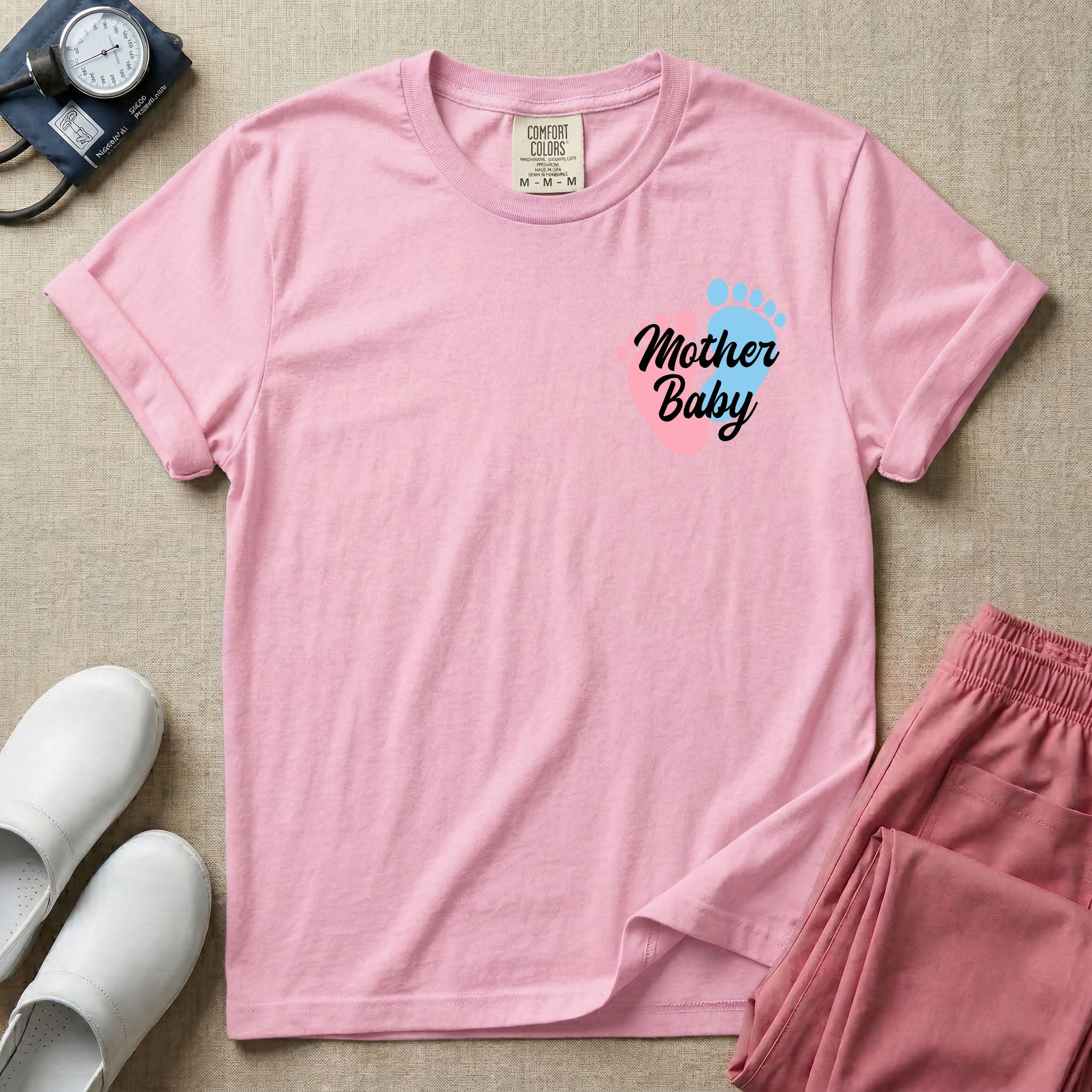 A minimalist postpartum nursing t-shirt featuring a small left chest graphic of two baby footprints, one pink and one blue, with the cursive white text "Mother Baby" written across them.