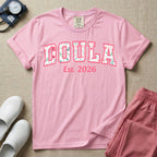 A personalized Doula graphic featuring the word DOULA in large, arched varsity-style letters filled with a delicate pink and green floral pattern, positioned above customizable text that reads Est. 2026.