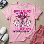 General nursing and ER t-shirt featuring a pink and black caduceus medical symbol flanked by two syringes alongside the humorous text "DON'T MESS WITH ME... I GET PAID TO STAB PEOPLE WITH SHARP OBJECTS".