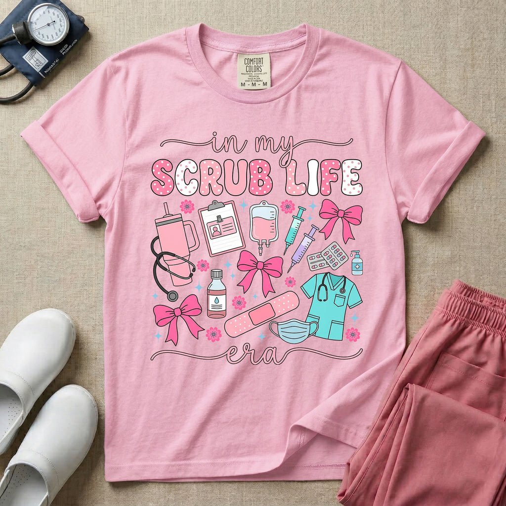 A cute general nursing t-shirt featuring the retro text "in my SCRUB LIFE era" surrounded by coquette medical graphics including a pink tumbler cup, stethoscope, IV bag with pink bows, clipboard, and blue scrubs.