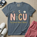 A humorous t-shirt for NICU nurses featuring the large text "NICU" in plaid and patterned letters with the phrase "Tiny Humans. Massive Attitudes." underneath, accompanied by small cute graphics of a syringe, an iced coffee cup, and a baby's face.