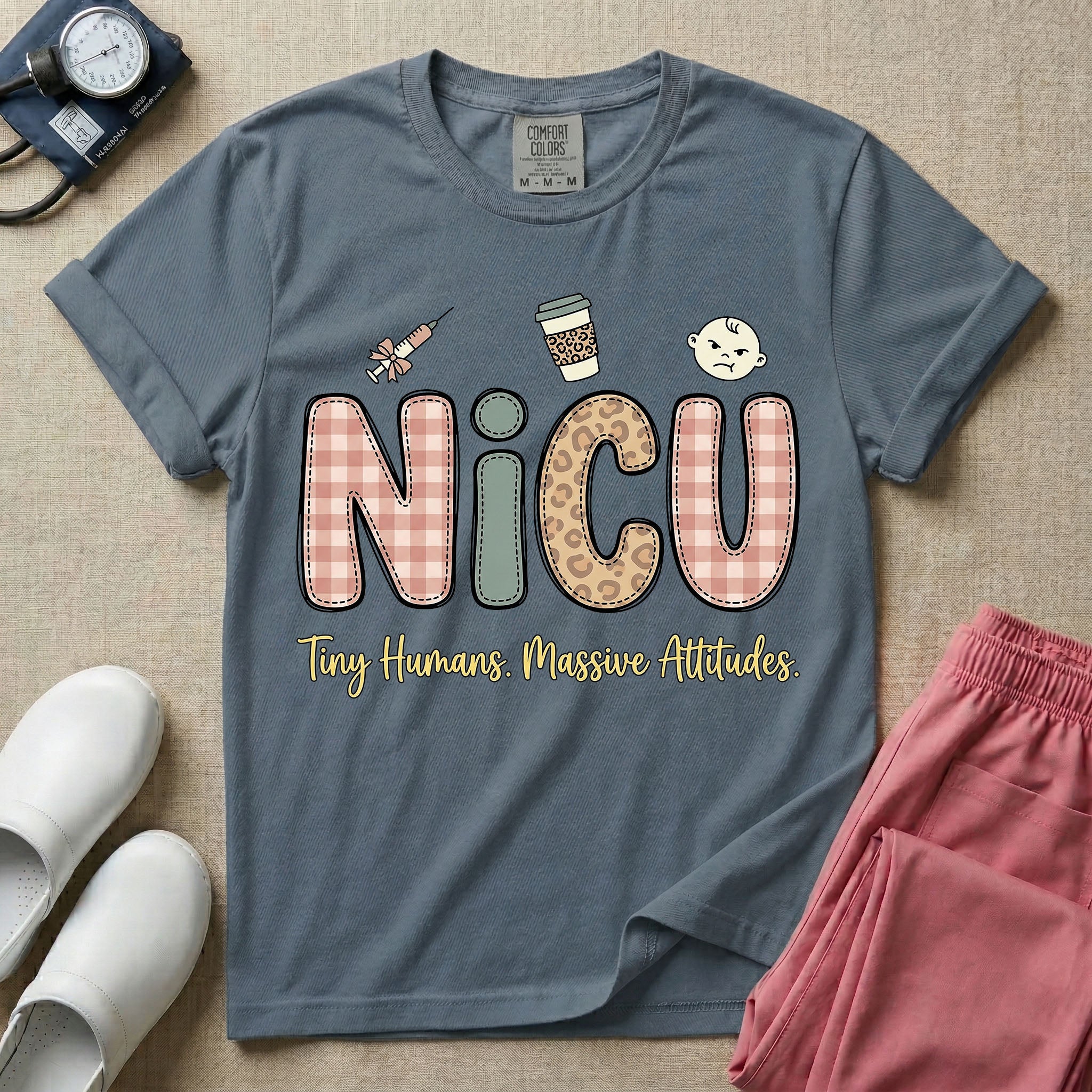 A humorous t-shirt for NICU nurses featuring the large text "NICU" in plaid and patterned letters with the phrase "Tiny Humans. Massive Attitudes." underneath, accompanied by small cute graphics of a syringe, an iced coffee cup, and a baby's face.