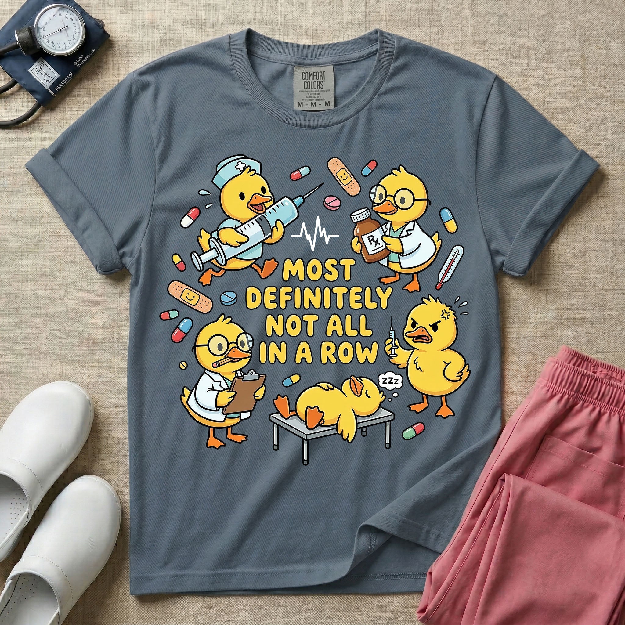 General nursing t-shirt featuring a chaotic group of cartoon ducklings dressed as medical professionals with the text "MOST DEFINITELY NOT ALL IN A ROW" on a sage green garment, in blue jean color.