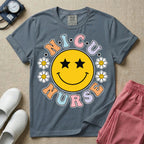 A t-shirt featuring a large yellow smiley face with star eyes surrounded by smiley face daisies and the text N.I.C.U. NURSE in pastel retro bubble lettering.