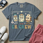 A retro-style t-shirt for emergency room nurses featuring the text "ER CREW" below a vintage cartoon illustration of a medicine bottle, a grumpy clipboard holding an AMA form, and a sandwich wearing a nurse cap walking together.