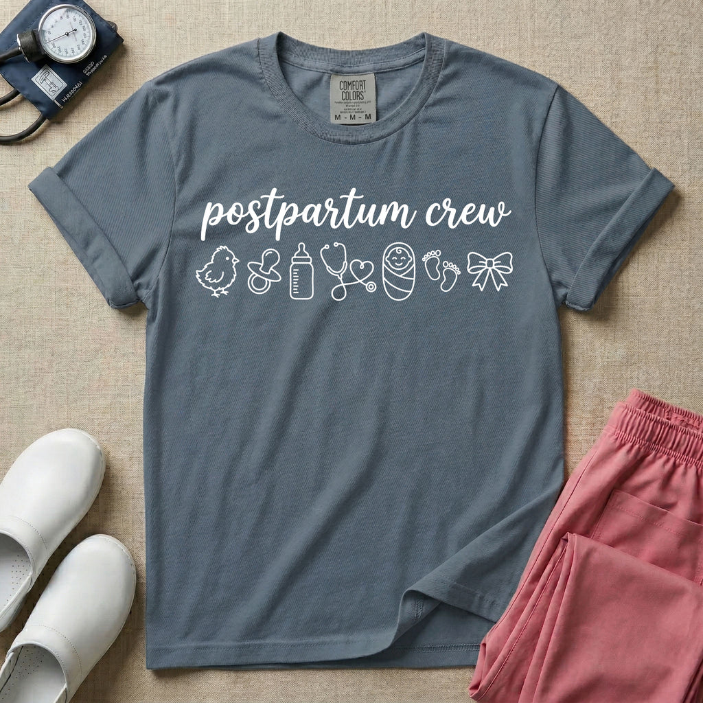 A t-shirt featuring the lowercase text postpartum crew in a cursive script font above a horizontal row of minimalist line-art icons including a baby chick, a pacifier, a baby bottle, a heart-shaped stethoscope, a swaddled baby, baby footprints, and a ribbon bow.