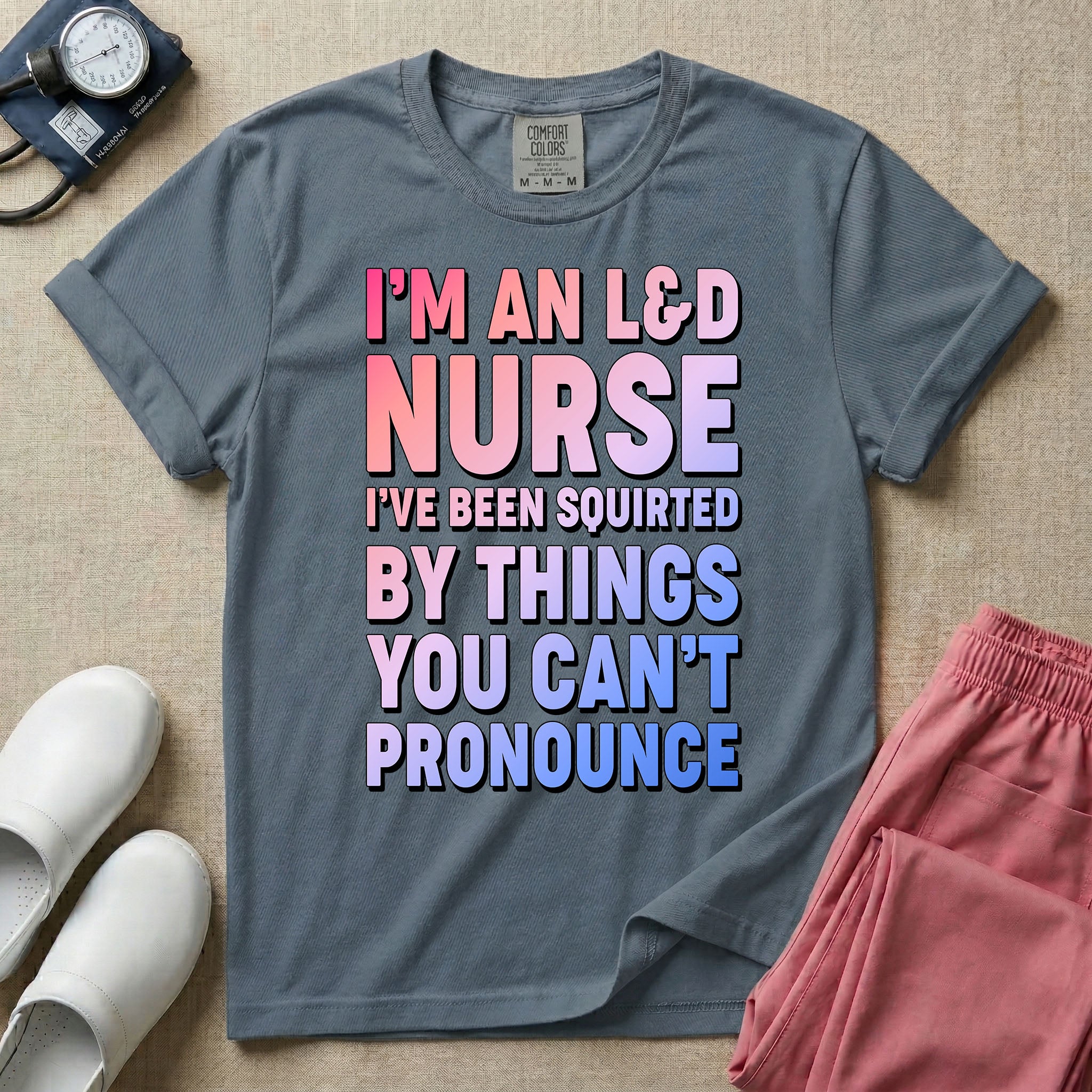A humorous graphic tee for labor and delivery nurses featuring bold, gradient block lettering that reads "I'M AN L&D NURSE I'VE BEEN SQUIRTED BY THINGS YOU CAN'T PRONOUNCE".