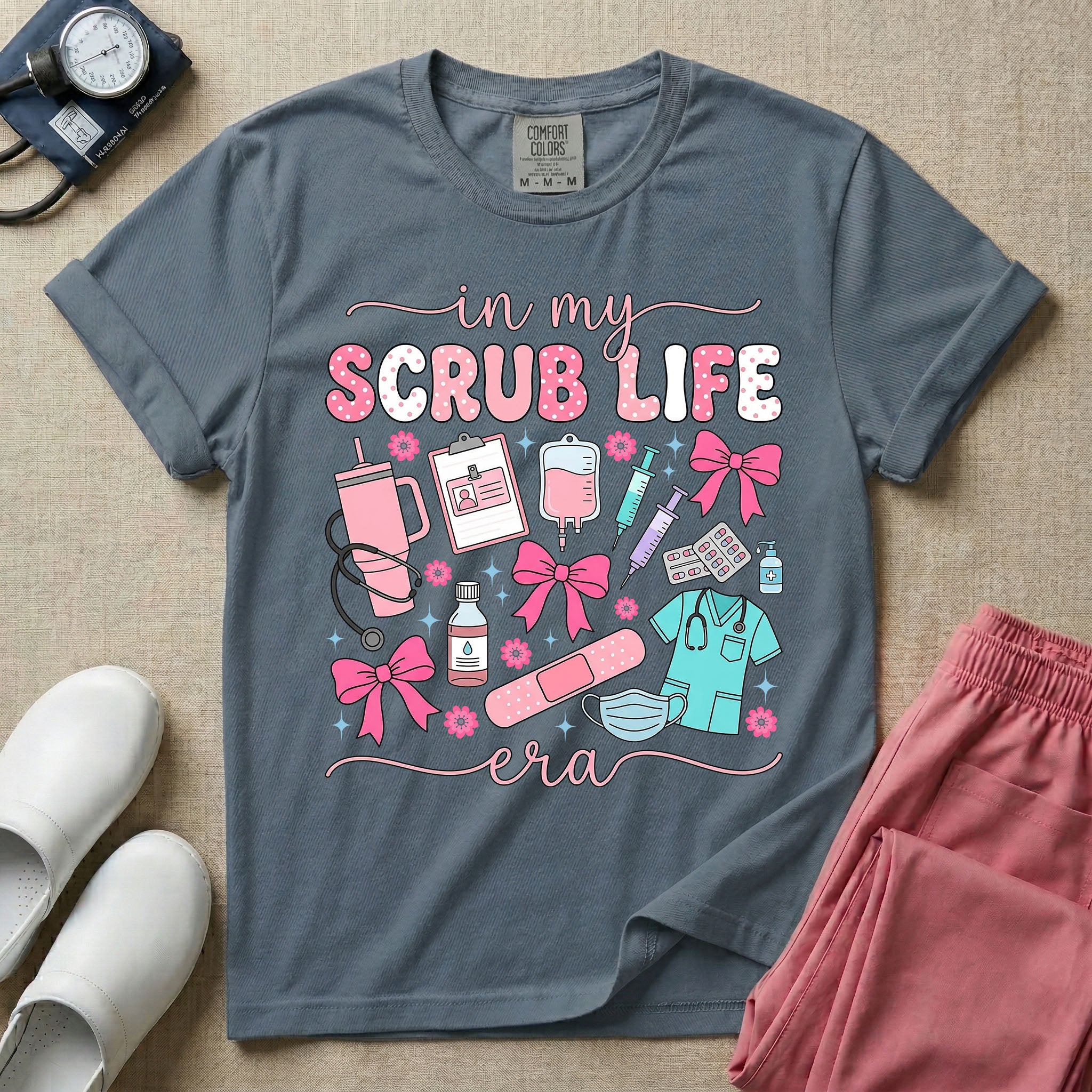 A cute general nursing t-shirt featuring the retro text "in my SCRUB LIFE era" surrounded by coquette medical graphics including a pink tumbler cup, stethoscope, IV bag with pink bows, clipboard, and blue scrubs.