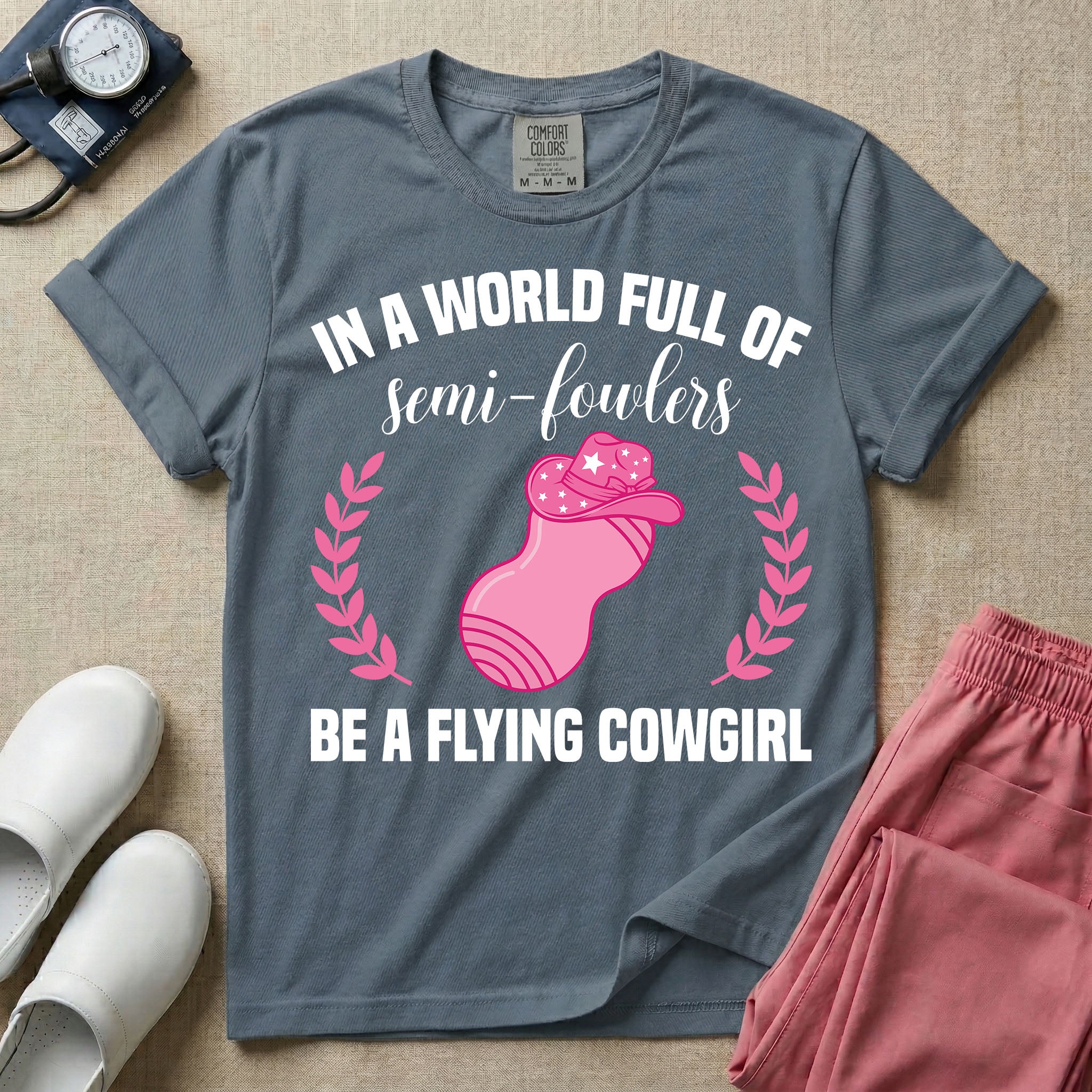 A humorous graphic tee for labor and delivery nurses featuring an illustration of a peanut ball wearing a cowboy hat, framed by laurel branches, along with the text "IN A WORLD FULL OF semi-fowlers BE A FLYING COWGIRL".