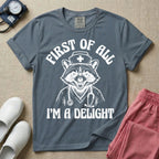 A humorous graphic of a raccoon dressed in a nursing cap and scrub jacket with a stethoscope, with the text "FIRST OF ALL I'M A DELIGHT", in blue jean color.