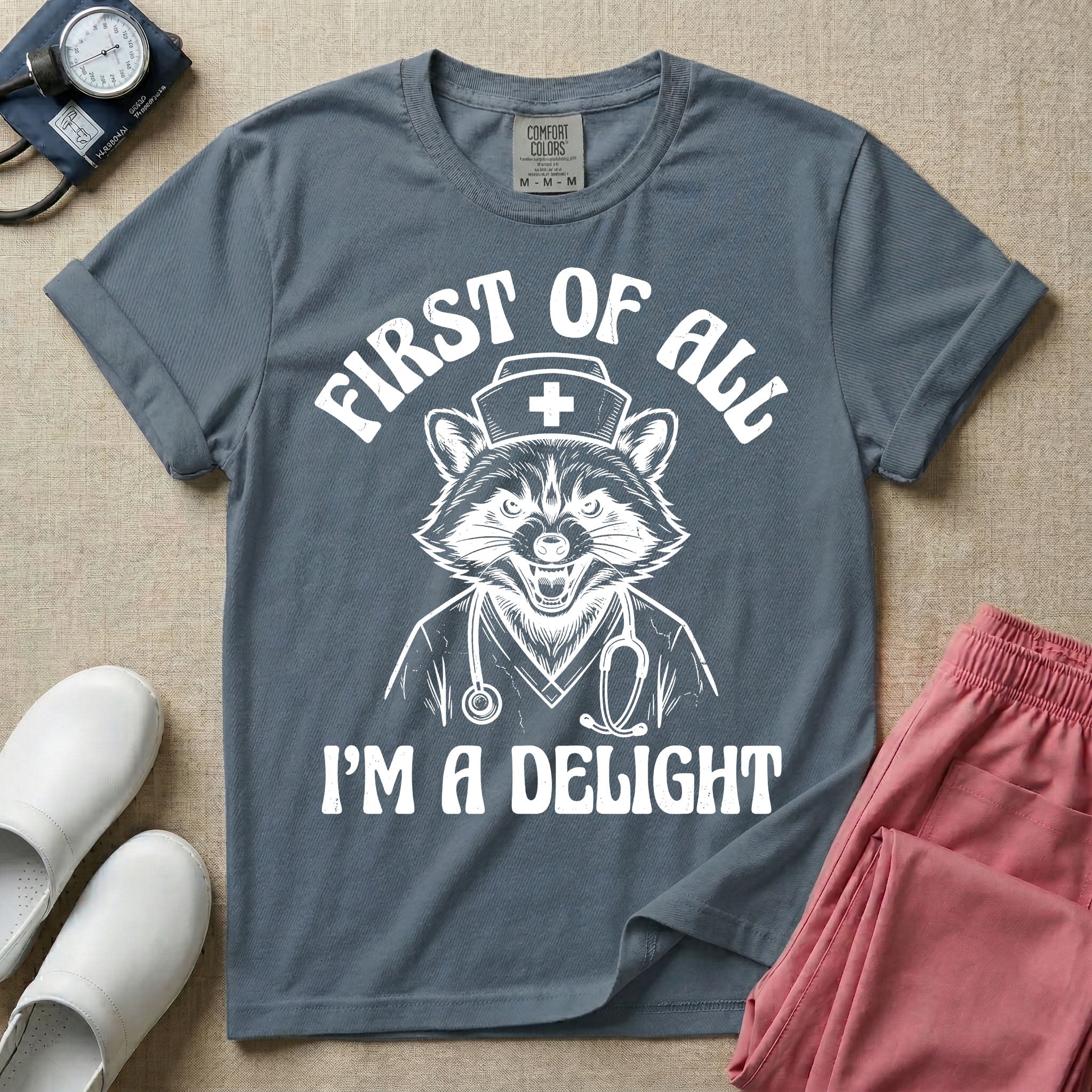 A humorous graphic of a raccoon dressed in a nursing cap and scrub jacket with a stethoscope, with the text "FIRST OF ALL I'M A DELIGHT", in blue jean color.