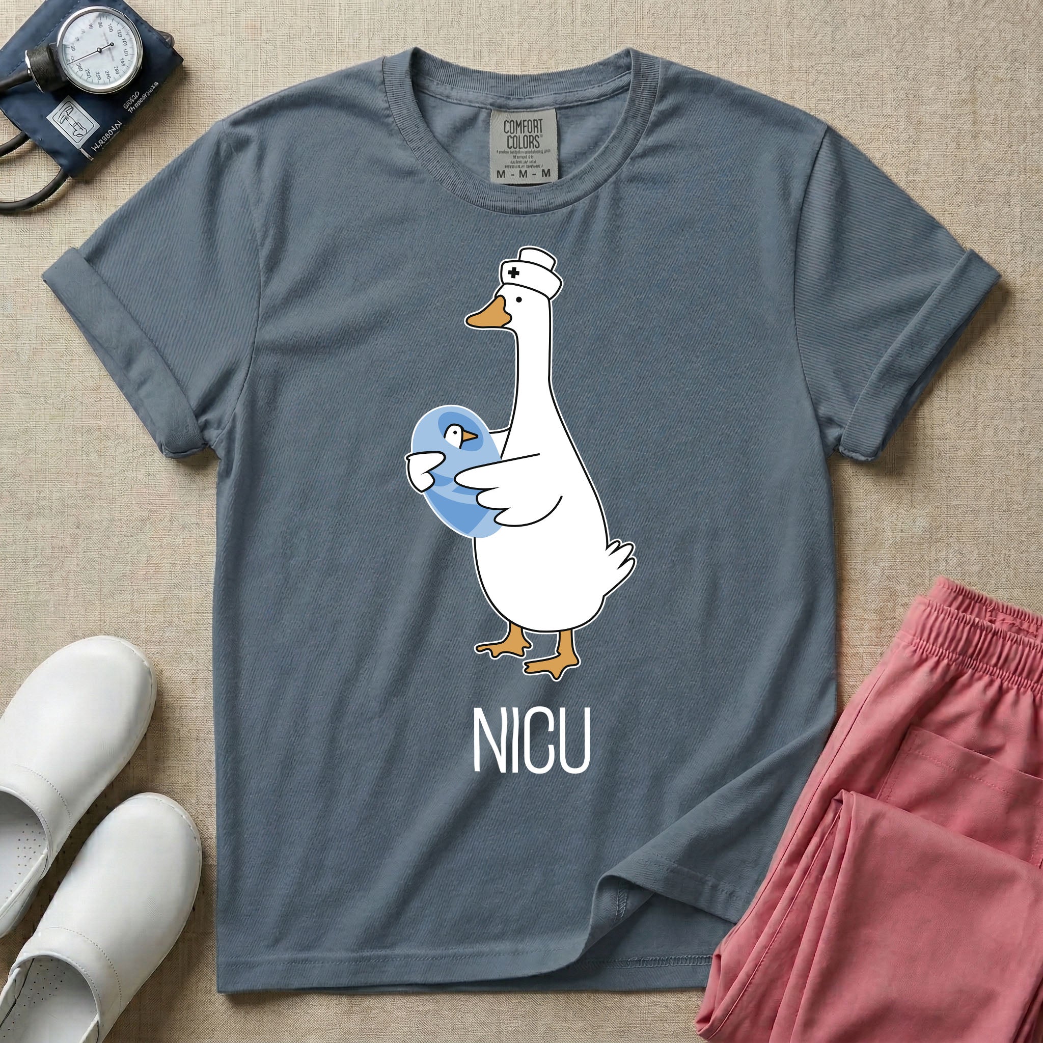 A t-shirt featuring an illustration of a white silly goose wearing a nurse's cap and holding a baby goose swaddled in a blue blanket, with the text NICU printed below.