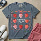 A funny and cute postpartum nursing t-shirt featuring the pun text "postpartum is my jam" surrounded by a graphic of red and pink strawberries, enclosed in a decorative wavy border with a bow at the top.