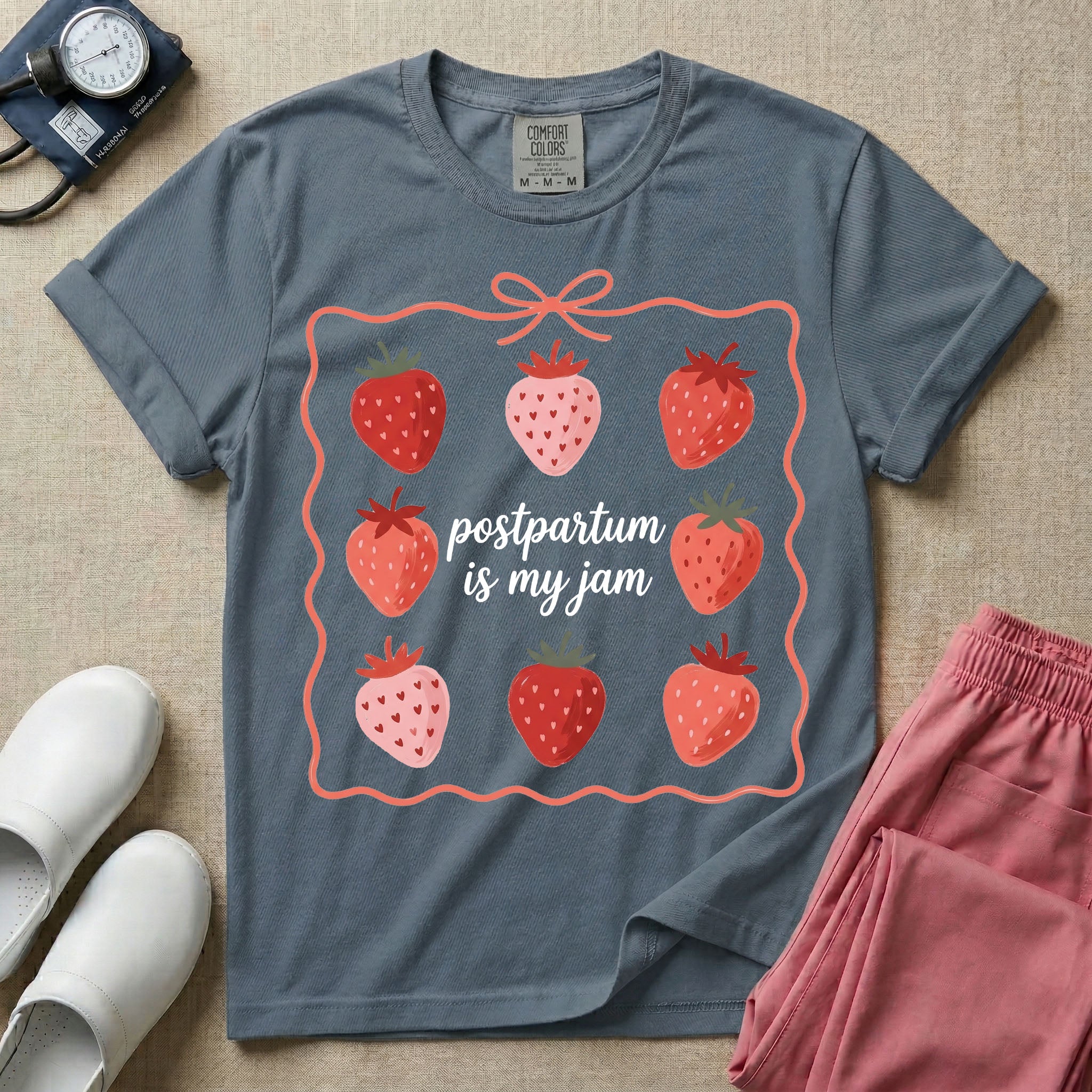 A funny and cute postpartum nursing t-shirt featuring the pun text "postpartum is my jam" surrounded by a graphic of red and pink strawberries, enclosed in a decorative wavy border with a bow at the top.