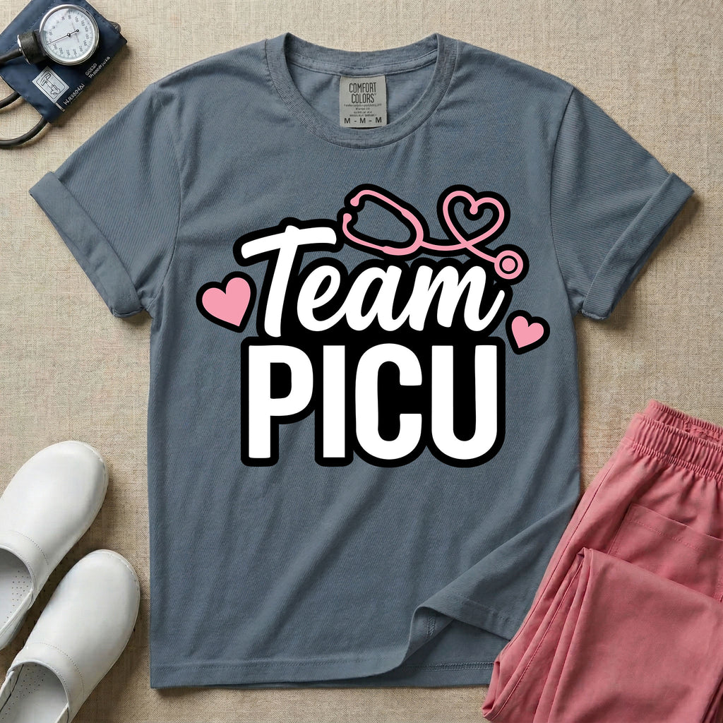 A descriptive graphic tee for pediatric intensive care nurses featuring the text "Team PICU" in bold white lettering, accented with pink hearts and a pink stethoscope design.