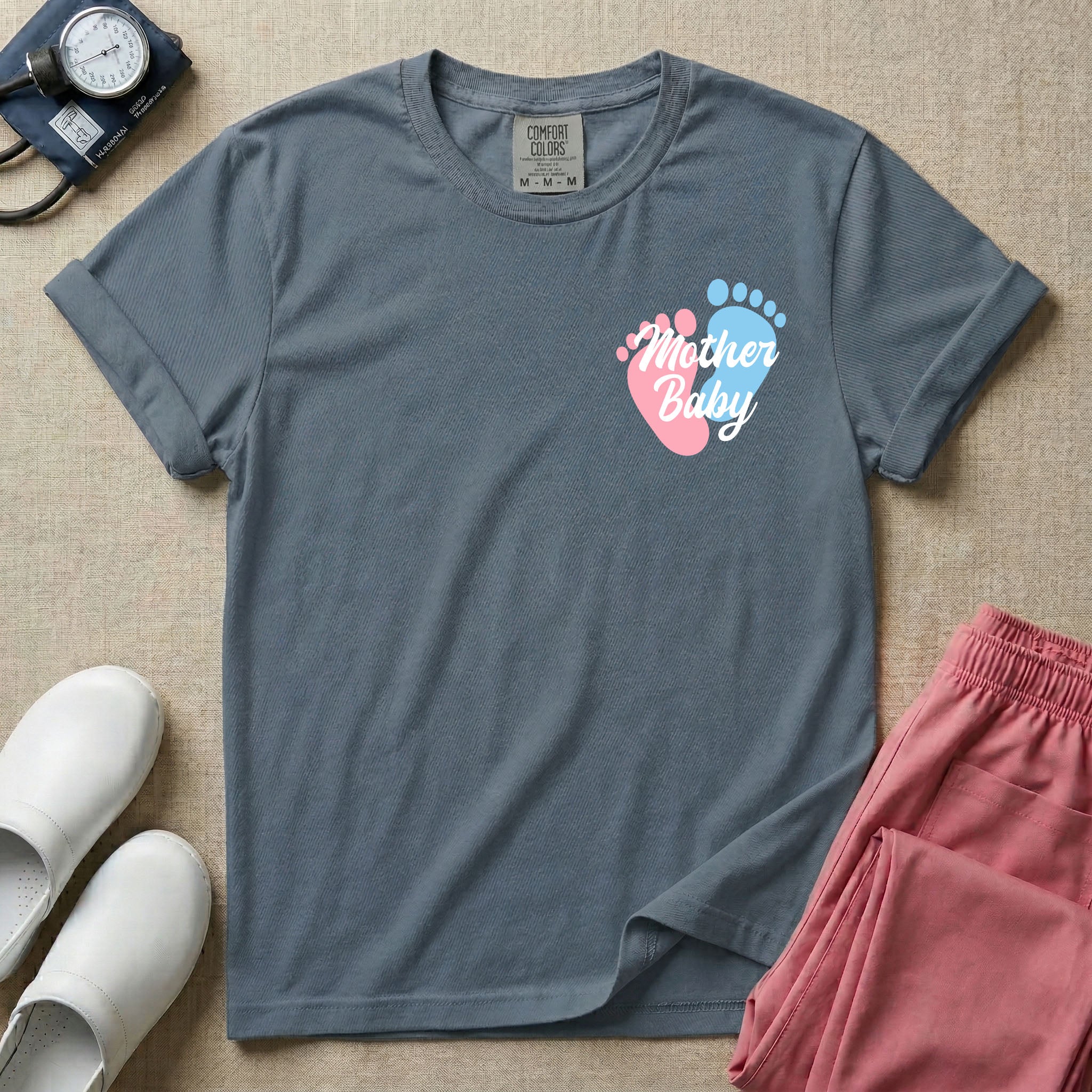 A minimalist postpartum nursing t-shirt featuring a small left chest graphic of two baby footprints, one pink and one blue, with the cursive white text "Mother Baby" written across them.