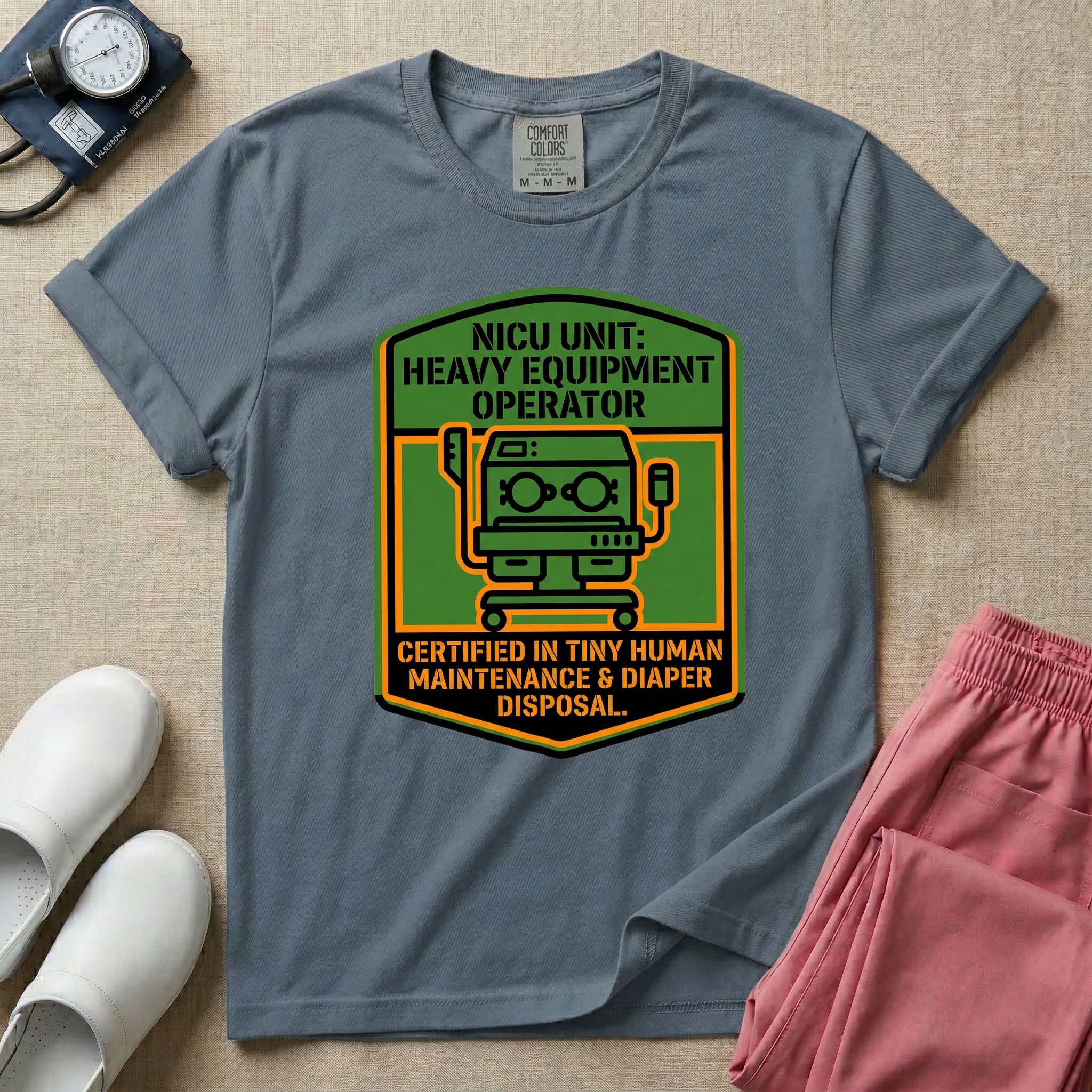 A graphic resembling a patch with green borders and orange inner sections featuring an illustration of a medical incubator in the center, with the text 'NICU UNIT: HEAVY EQUIPMENT OPERATOR' at the top and 'CERTIFIED IN TINY HUMAN MAINTENANCE & DIAPER DISPOSAL' at the bottom.