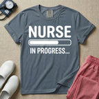 General nursing student t-shirt featuring a white loading bar graphic and the text "NURSE IN PROGRESS..." on a dark gray garment, in blue jean color.