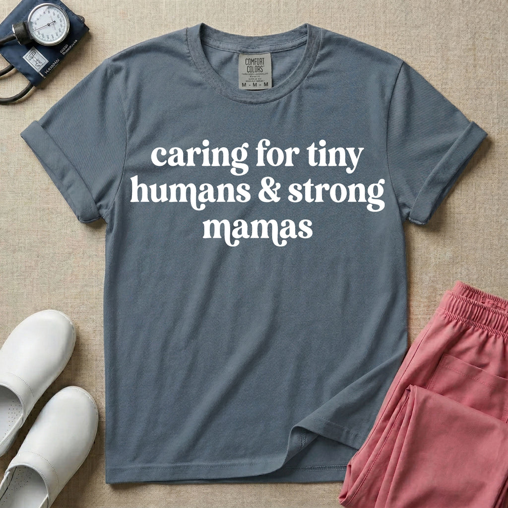 A minimalist nursing t-shirt featuring the text "caring for tiny humans & strong mamas" written in a retro white serif font.