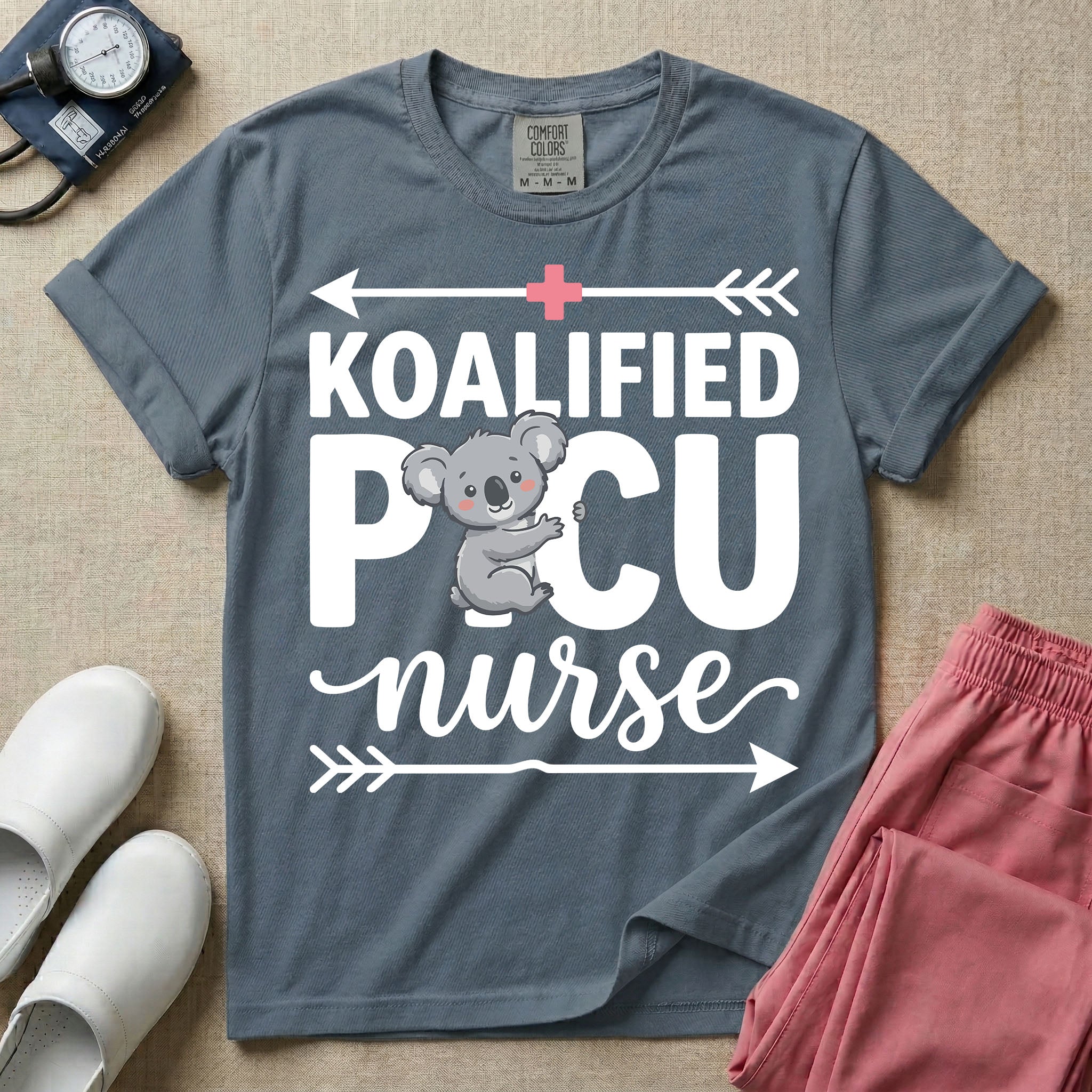 A funny pediatric intensive care nursing t-shirt featuring the pun text "KOALIFIED PICU nurse" with a cute koala graphic replacing the letter I in PICU, framed by decorative arrows and a pink medical cross.