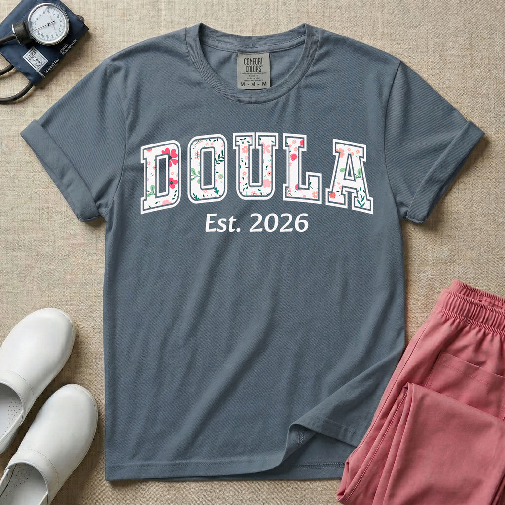 A personalized Doula graphic featuring the word DOULA in large, arched varsity-style letters filled with a delicate pink and green floral pattern, positioned above customizable text that reads Est. 2026.