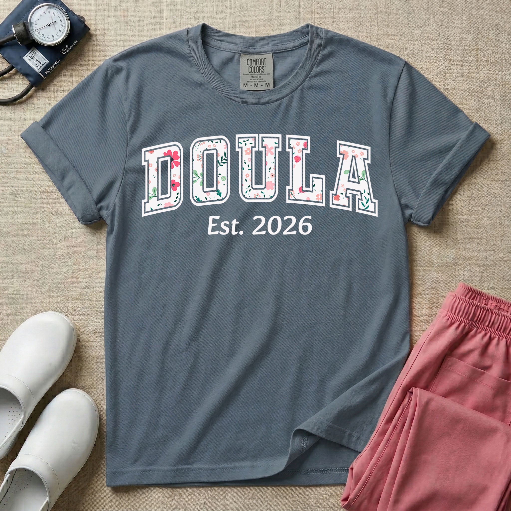 A personalized Doula graphic featuring the word DOULA in large, arched varsity-style letters filled with a delicate pink and green floral pattern, positioned above customizable text that reads Est. 2026.