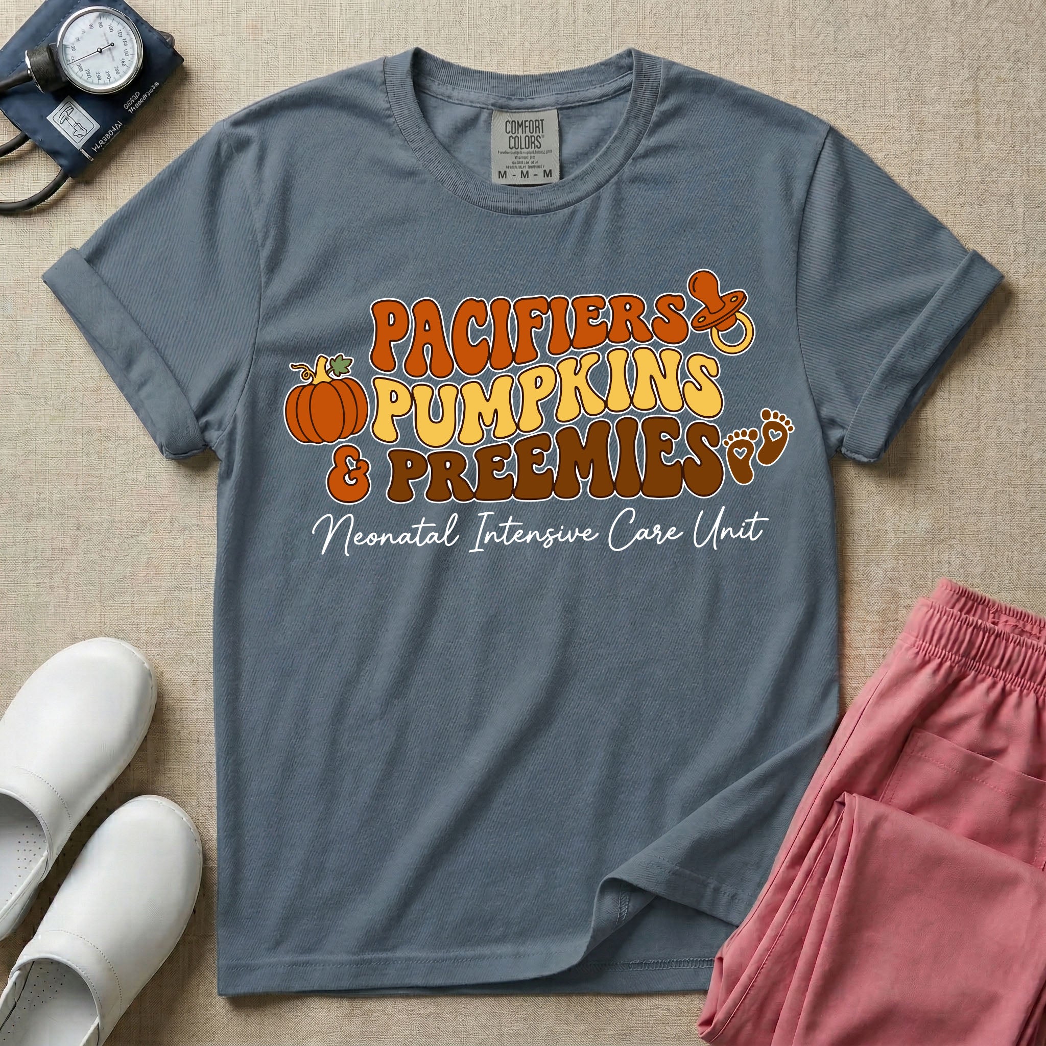 A t-shirt featuring the stacked text PACIFIERS PUMPKINS & PREEMIES in wavy orange, yellow, and brown retro lettering decorated with a pumpkin, pacifier, and baby footprints, with Neonatal Intensive Care Unit written in cursive below.