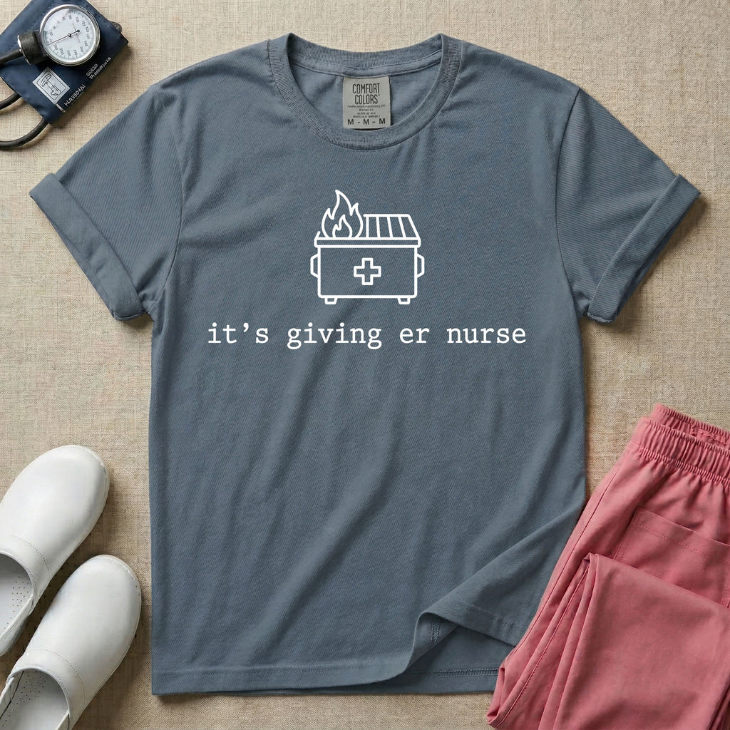 A funny minimalist ER nursing t-shirt featuring a simple white line drawing of a dumpster on fire with a medical cross on it, sitting above the lower-case typewriter text "it's giving er nurse".