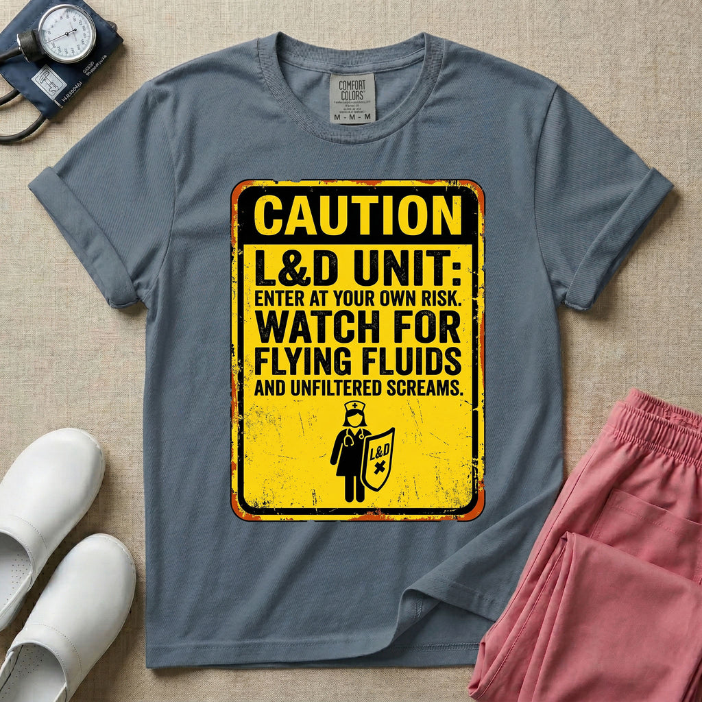 A humorous graphic tee for labor and delivery nurses featuring a distressed caution sign design with the text "CAUTION L&D UNIT: ENTER AT YOUR OWN RISK. WATCH FOR FLYING FLUIDS AND UNFILTERED SCREAMS." above a stick figure nurse holding a shield.