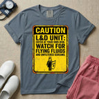 A humorous graphic tee for labor and delivery nurses featuring a distressed caution sign design with the text "CAUTION L&D UNIT: ENTER AT YOUR OWN RISK. WATCH FOR FLYING FLUIDS AND UNFILTERED SCREAMS." above a stick figure nurse holding a shield.