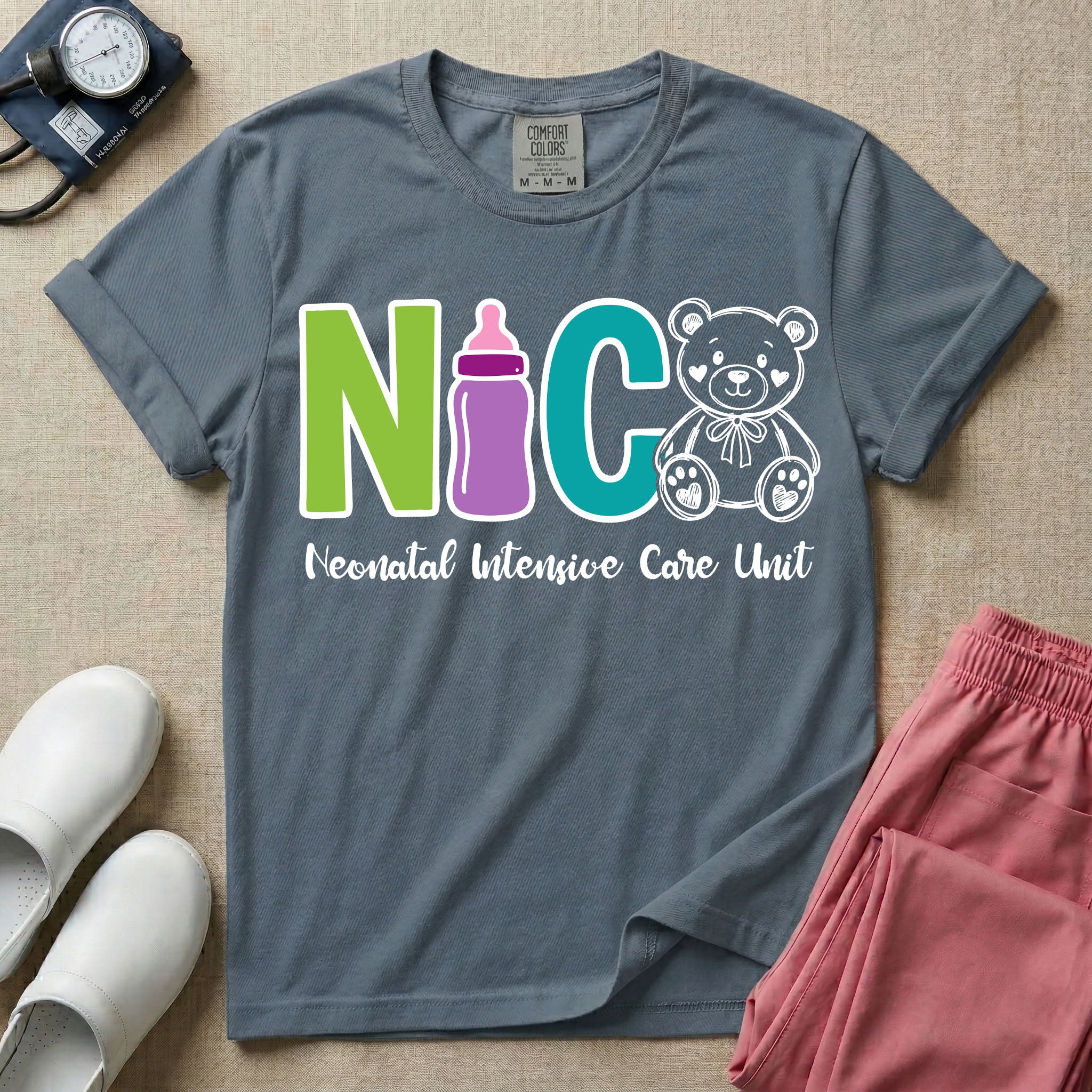 A t-shirt featuring the acronym NICU creatively spelled out using a green letter N, a purple baby bottle, a teal letter C, and a white outlined teddy bear, with the words Neonatal Intensive Care Unit written in cursive script below.