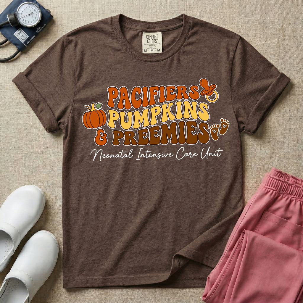 A t-shirt featuring the stacked text PACIFIERS PUMPKINS & PREEMIES in wavy orange, yellow, and brown retro lettering decorated with a pumpkin, pacifier, and baby footprints, with Neonatal Intensive Care Unit written in cursive below.