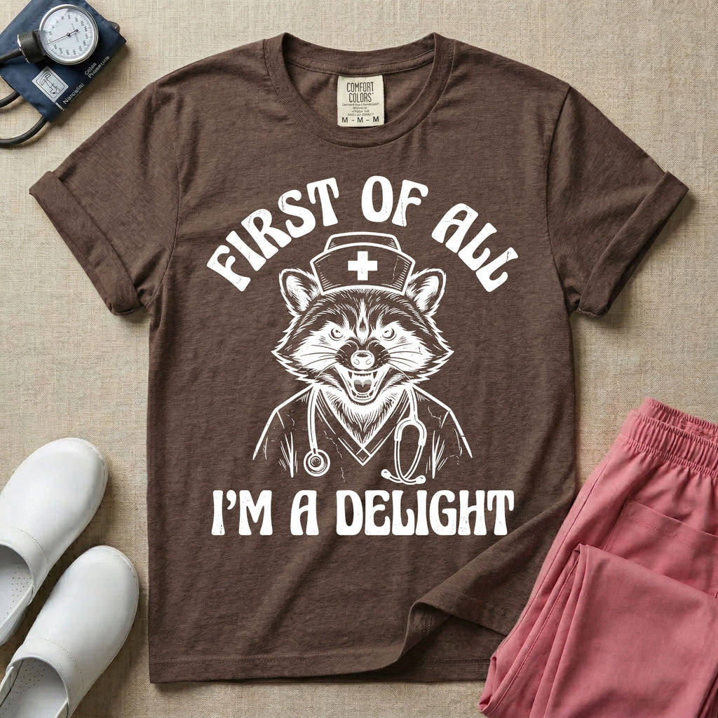 A humorous graphic of a raccoon dressed in a nursing cap and scrub jacket with a stethoscope, with the text "FIRST OF ALL I'M A DELIGHT", in espresso color.