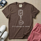 A funny minimalist ER nursing t-shirt featuring a white line drawing of an IV bag containing a coffee bean dripping into a mug labeled "night shift", sitting above the lower-case typewriter text "it's giving er nurse".