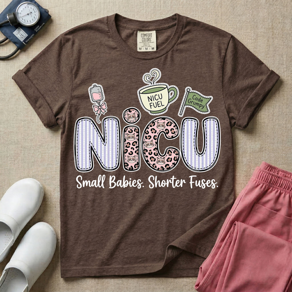 A funny t-shirt for NICU nurses featuring the large text "NICU" patterned with purple stripes and pink leopard print containing grumpy cat faces, accompanied by graphics of an IV bag with a pink bow, a steaming coffee cup reading "NICU FUEL", a green flag saying "Code Grumpy", and the bottom text "Small Babies. Shorter Fuses."