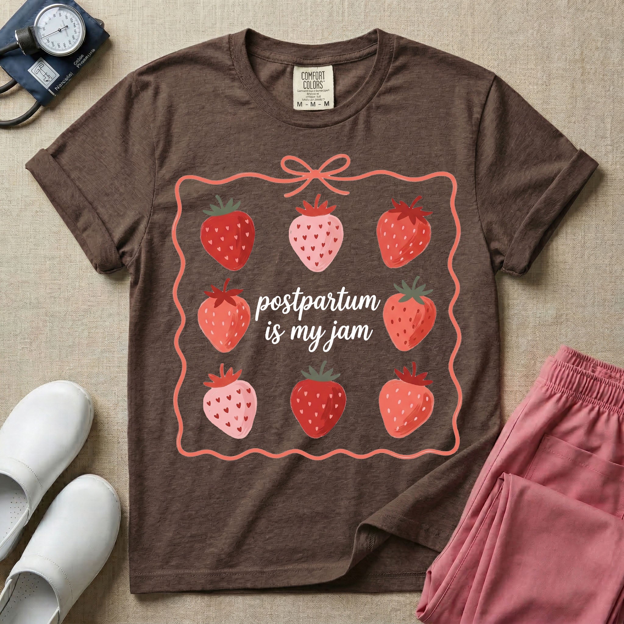 A funny and cute postpartum nursing t-shirt featuring the pun text "postpartum is my jam" surrounded by a graphic of red and pink strawberries, enclosed in a decorative wavy border with a bow at the top.