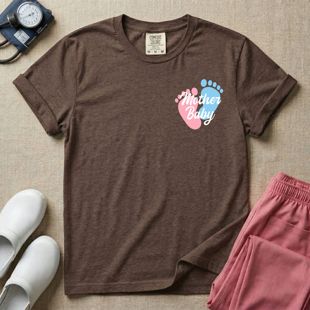 A minimalist postpartum nursing t-shirt featuring a small left chest graphic of two baby footprints, one pink and one blue, with the cursive white text "Mother Baby" written across them.