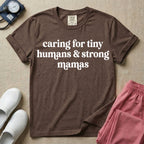 A minimalist nursing t-shirt featuring the text "caring for tiny humans & strong mamas" written in a retro white serif font.