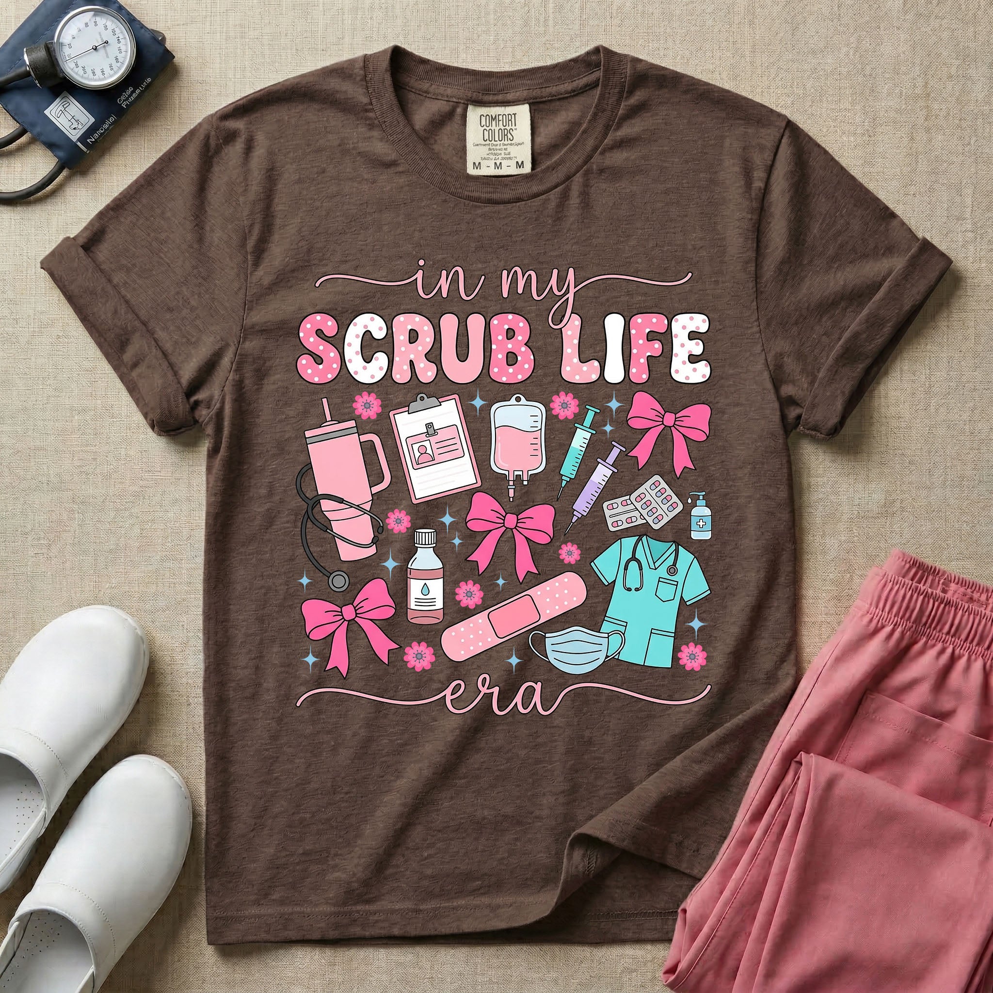 A cute general nursing t-shirt featuring the retro text "in my SCRUB LIFE era" surrounded by coquette medical graphics including a pink tumbler cup, stethoscope, IV bag with pink bows, clipboard, and blue scrubs.