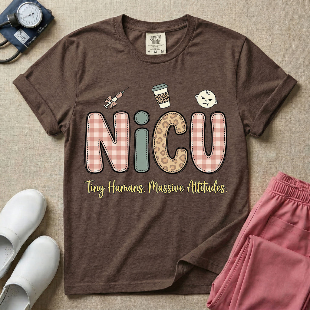 A humorous t-shirt for NICU nurses featuring the large text "NICU" in plaid and patterned letters with the phrase "Tiny Humans. Massive Attitudes." underneath, accompanied by small cute graphics of a syringe, an iced coffee cup, and a baby's face.